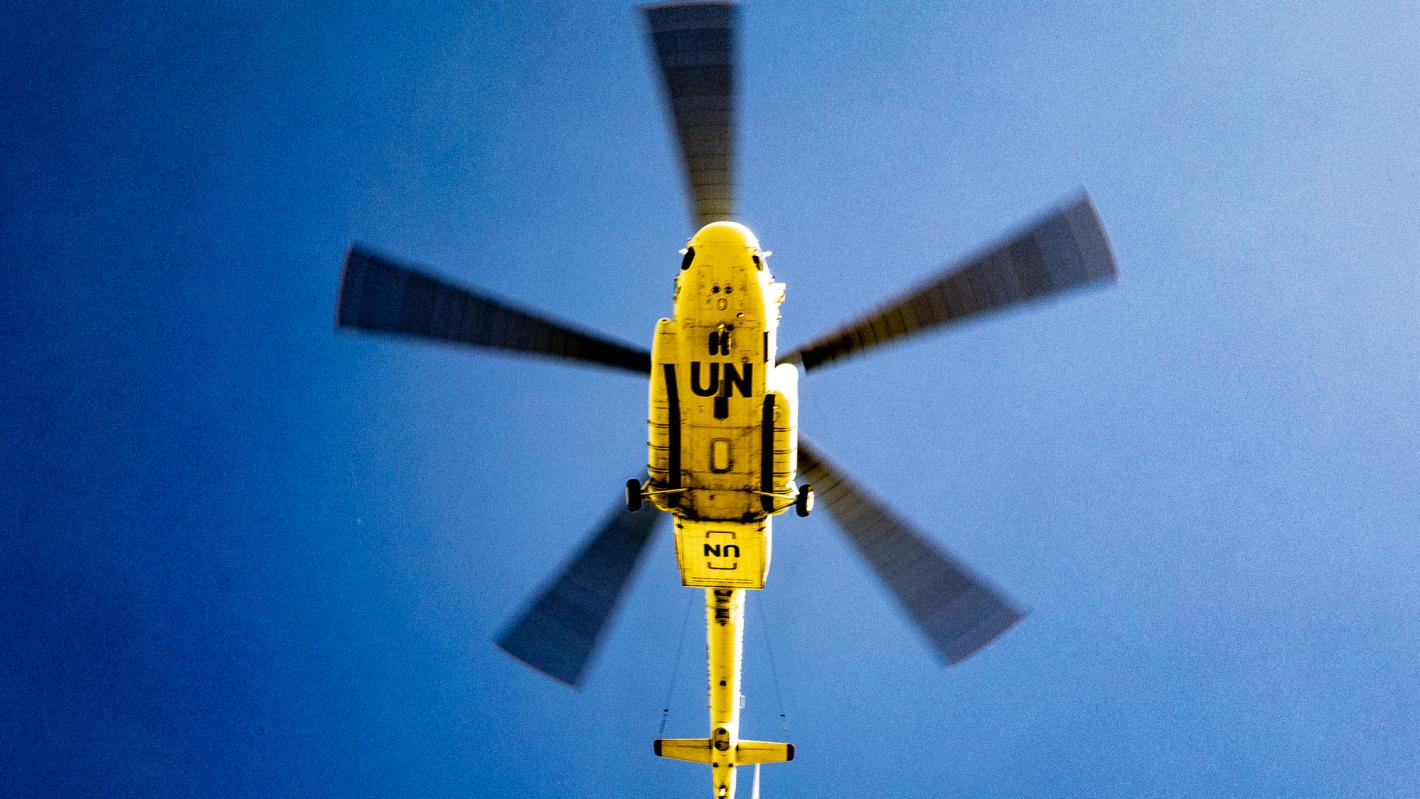 The underside of a yellow UN helicopter against a blue sky